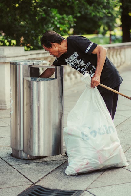 A large pile of black plastic rubbish bags, some torn open revealing plastic bottles and miscellaneous waste, stacked against a wall with metallic and tiled finishes. The bags are situated outdoors on